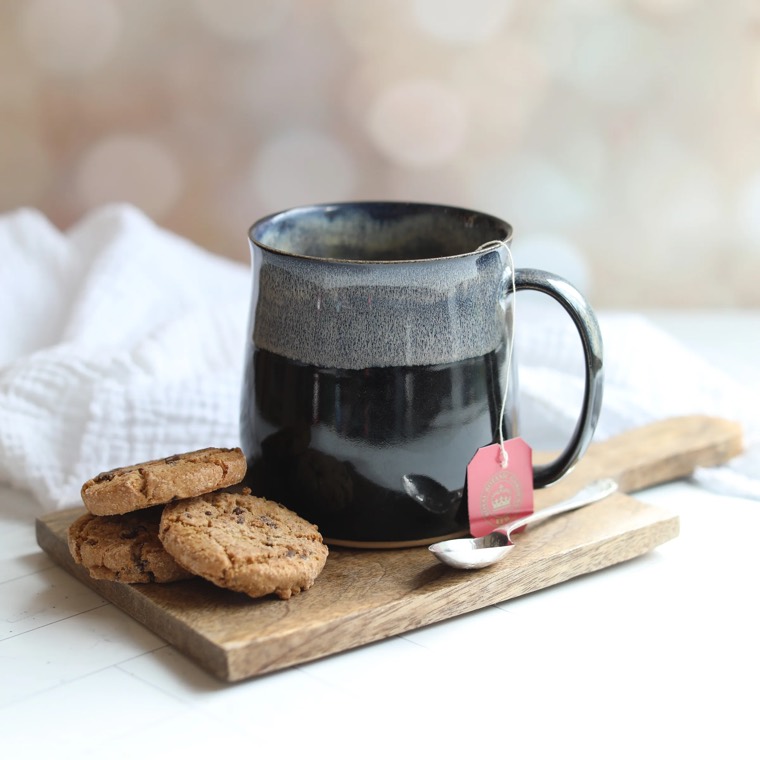 Handmade speckled stoneware coffee mug on a wooden board with cookies